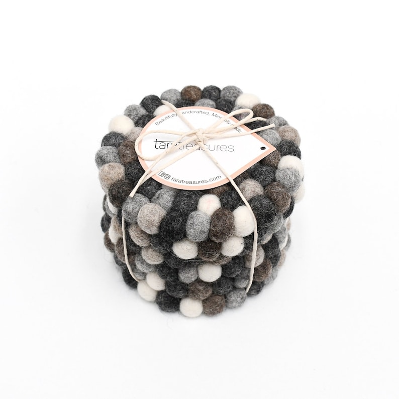 May include: Set of four gray, brown, and white felt coasters with a round shape. The coasters are made of small, round balls of felt. The coasters are stacked on top of each other. The coasters are tied together with a string and a tag that says "tara treasures".