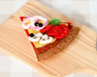 May include: A felt pizza slice with red pepper, mushrooms, and onion toppings on a wooden cutting board.