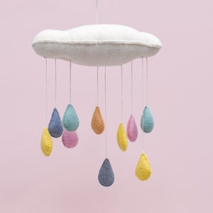 May include: A white felt cloud mobile with colourful felt raindrops hanging from it. The raindrops are in shades of yellow, pink, blue, and green.