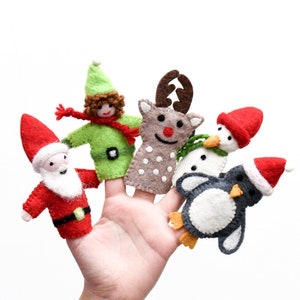 Pode incluir: Cinco fantoches de dedo de feltro que representam personagens natalinos: Papai Noel, um duende, uma rena, um pinguim e um boneco de neve. Os fantoches estão todos vestidos com cores festivas e têm rostos amigáveis.