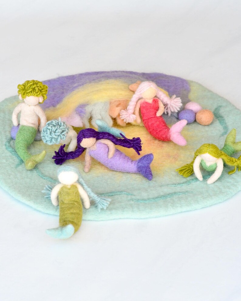 May include: A set of felt mermaid dolls on a rainbow-colored felt play mat. The mermaids are in various colors, including green, pink, purple, and blue. The play mat is a circle with a light blue border and a rainbow-colored center.