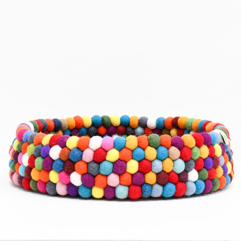 May include: A round, multi-colored felt ball basket. The basket is made of rows of colorful felt balls in shades of red, orange, yellow, green, blue, purple, and white. The basket is a vibrant and decorative item.