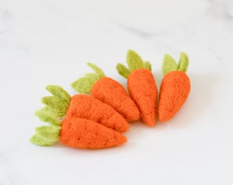 May include: Five orange felt carrots with green felt tops are arranged on a white marble surface. The carrots are a bright orange color and have a slightly textured appearance. The green tops have a leaf-like shape.