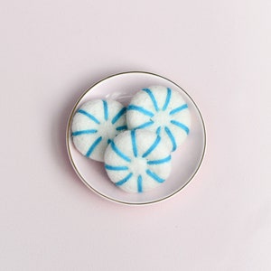 May include: Three white felt peppermint sweets with blue stripes on a pink saucer.