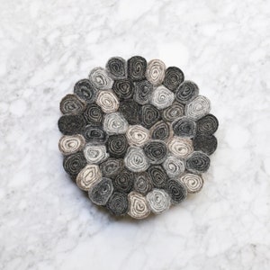 May include: A round, grey and beige wool rug made of many small, rolled circles.
