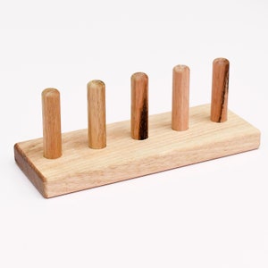 May include: Wooden toy with five dowels, each with a different length, mounted on a rectangular base. The dowels are made of natural wood and have a light brown color.