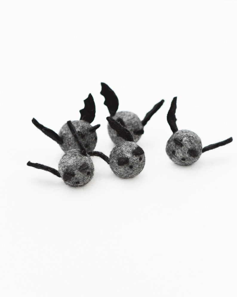 May include: Six gray felt bat ornaments with black felt wings and faces. The bats are arranged in a cluster on a white background.