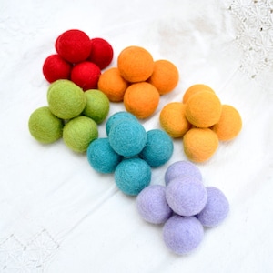 Puede incluir: Un conjunto de bolas de fieltro de colores en un patrón de arcoíris. Las bolas están dispuestas en forma de pirámide, con las bolas rojas en la parte superior y las bolas moradas en la parte inferior.
