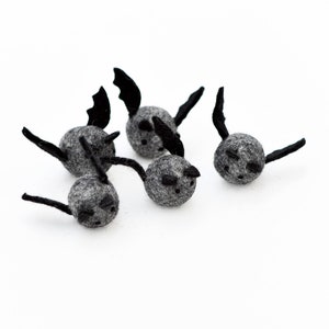 May include: Five gray felt bats with black felt wings. The bats are small and round, with black eyes and a small black mouth.
