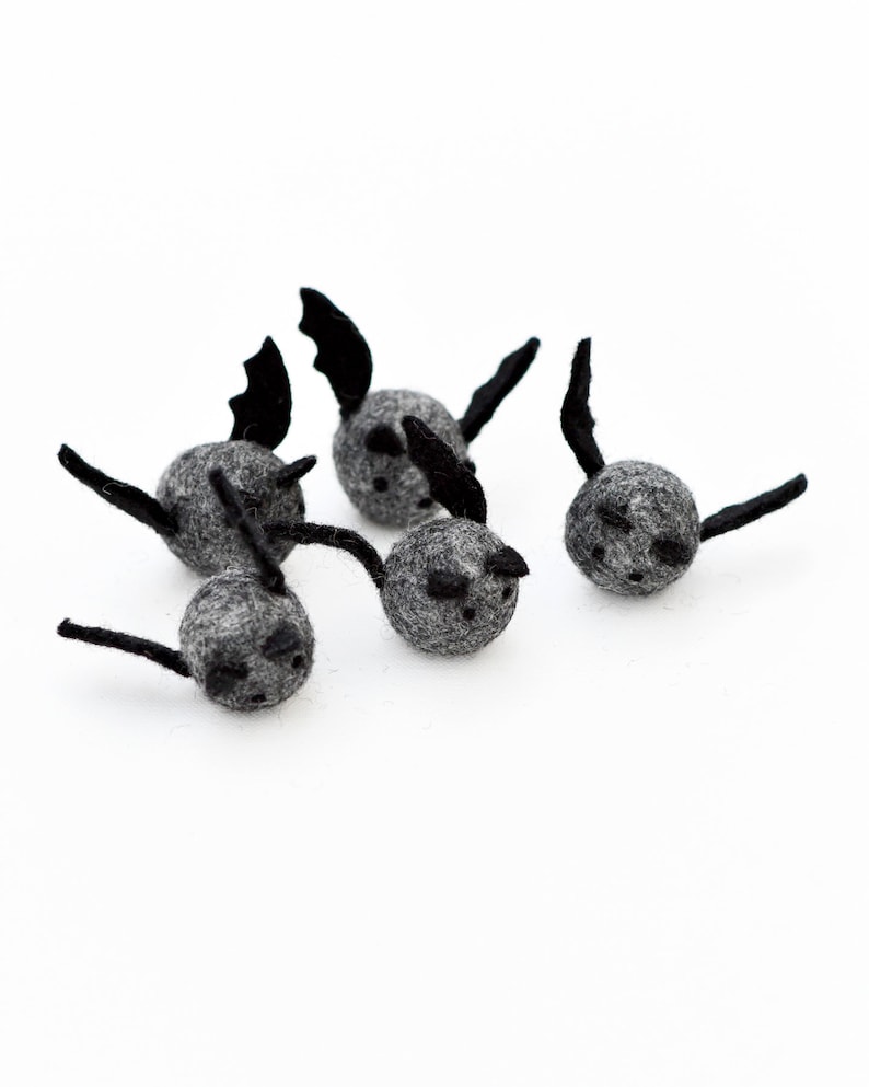 May include: Five gray felt bats with black felt wings. The bats are small and round, with black eyes and a small black mouth.
