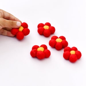 May include: Five felt flower embellishments in red with yellow centers. The flowers are arranged in a row on a white surface.