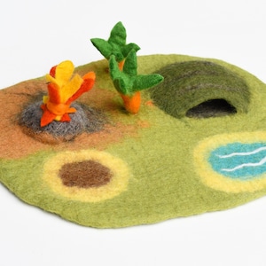 May include: A felt play mat with a green grassy surface, a brown cave, a blue pond, a yellow and orange fire, and two green palm trees.
