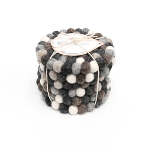 May include: Set of six gray, brown, and white felt coasters with a textured ball design. The coasters are stacked and tied together with twine. The label reads "Tara Treasures".