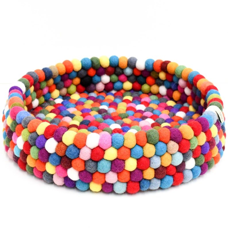 May include: A round pet bed crafted from colorful felt balls. The bed features a vibrant mix of red, orange, yellow, green, blue, purple, and white balls, creating a textured surface. The bed's design is suitable for small pets.