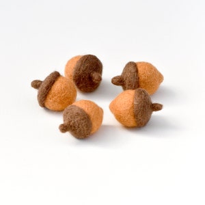 May include: Five felt acorns in brown and orange colors. The acorns are arranged in a circle on a white background.