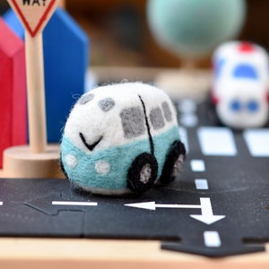 May include: A white and blue felt toy car with a smiling face. The car is on a black felt road with white lines.