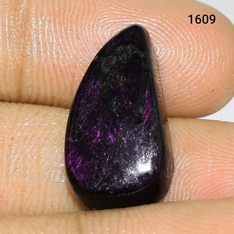 K&ouml;nnte beinhalten: Ein tropfenf&ouml;rmiger Cabochon-Edelstein in tiefem Lila und Schwarz. Der Stein hat einen schimmernden, irisierenden Effekt.