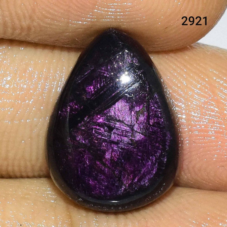 Puede incluir: Una piedra preciosa p&uacute;rpura en forma de l&aacute;grima con un brillo iridiscente oscuro. La piedra tiene un patr&oacute;n estriado &uacute;nico.