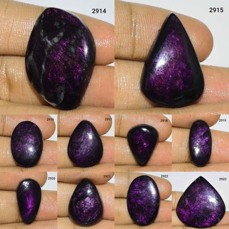 Puede incluir: Una colecci&oacute;n de diez cabujones de piedras preciosas iridiscentes de color p&uacute;rpura y negro, cada uno con una forma y un tama&ntilde;o &uacute;nicos. Los cabujones se muestran en una mano, con los n&uacute;meros 2914, 2915, 2916, 2917, 2918, 2919, 2920, 2921, 2922 y 2923 visibles en la imagen.