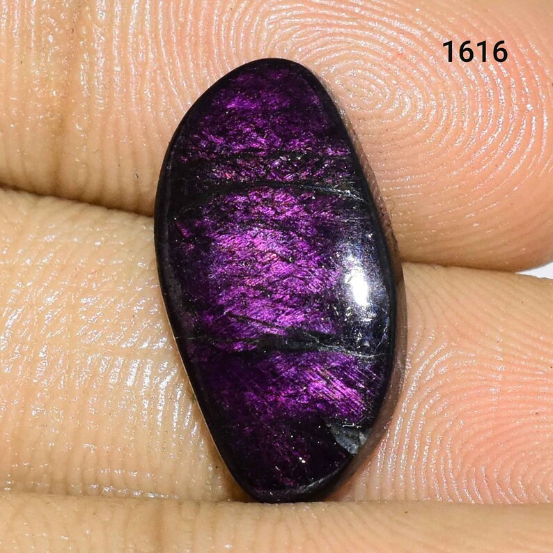 K&ouml;nnte beinhalten: Ein ovaler Edelstein in Lila und Schwarz mit schimmerndem, irisierendem Finish. Der Stein ist etwa 2,5 cm lang und 1,25 cm breit.