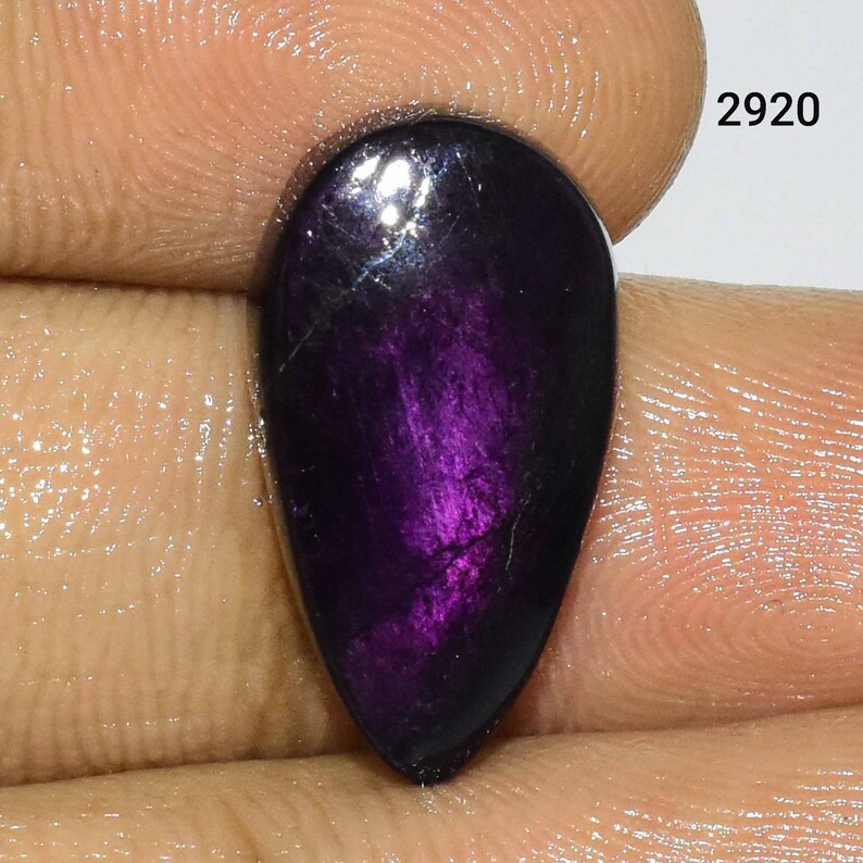 Puede incluir: Una piedra preciosa p&uacute;rpura en forma de l&aacute;grima con un efecto brillante e iridiscente. La piedra preciosa mide aproximadamente 2,5 cm de largo y 1,5 cm de ancho.