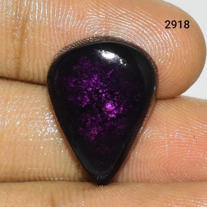 Puede incluir: Una piedra preciosa de color p&uacute;rpura oscuro con forma de l&aacute;grima y un acabado brillante e iridiscente.
