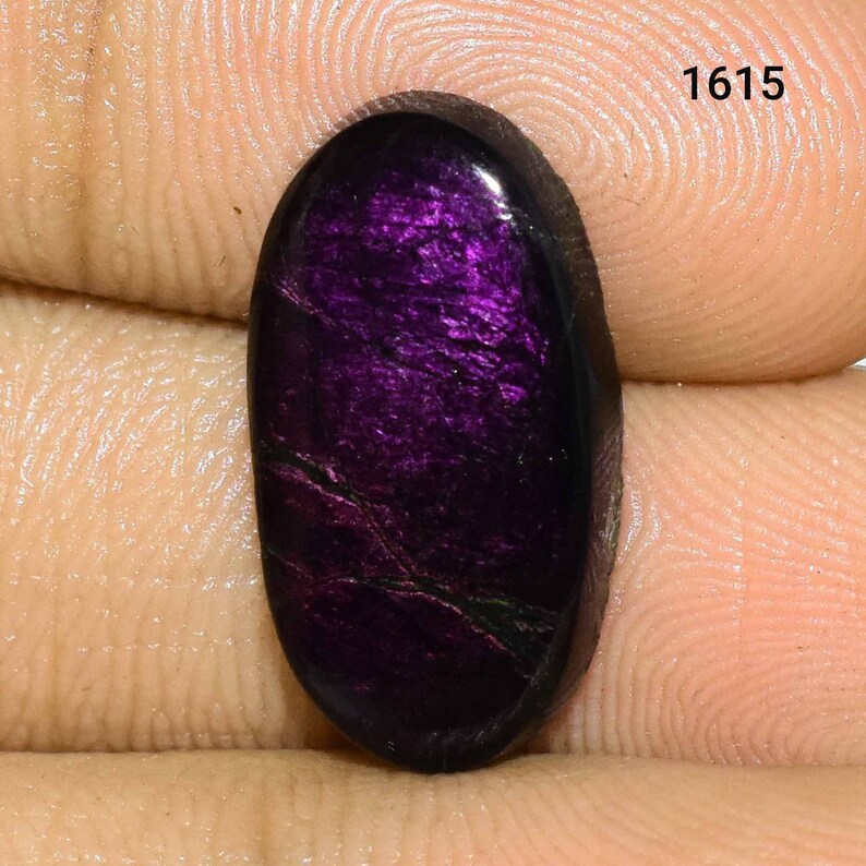 K&ouml;nnte beinhalten: Ein ovaler Cabochon-Edelstein in tiefem Lila mit irisierendem Schimmer und schwarzen Adern.