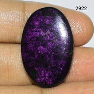 Puede incluir: Una piedra preciosa ovalada cabuj&oacute;n de color p&uacute;rpura oscuro con brillo iridiscente. La piedra tiene un fondo negro con motas p&uacute;rpuras y plateadas.