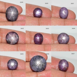 May include: Nine oval-shaped star ruby gemstones with a variety of colors, including purple, pink, and gray. The stones are arranged in three rows of three, with each stone labeled with a number.