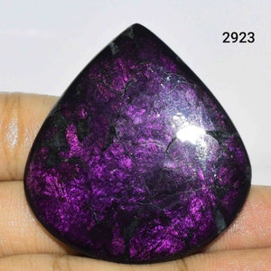 Puede incluir: Un cabuj&oacute;n de piedra preciosa de color morado oscuro y negro con forma de l&aacute;grima. La piedra tiene un acabado brillante e iridiscente.