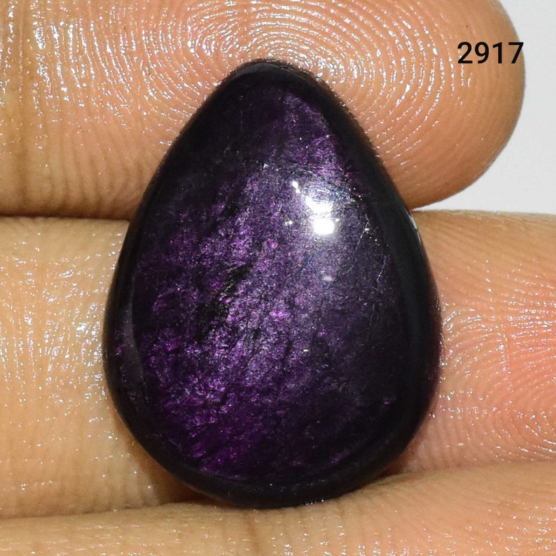 Puede incluir: Una piedra preciosa en forma de l&aacute;grima, de color p&uacute;rpura, con un acabado brillante e iridiscente. La piedra es lisa y pulida, con un color profundo y rico.