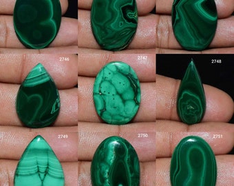 Puede incluir: Nueve cabujones de malaquita verde de forma ovalada y de gota, cada uno con patrones y vetas únicos. Las piedras están dispuestas en una cuadrícula en una mano.