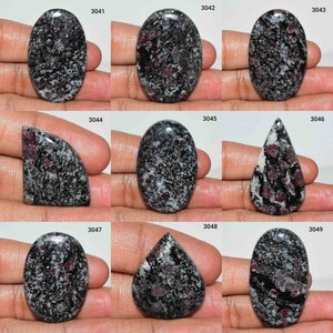 May include: Nine oval and teardrop shaped cabochons of black, white, and pink speckled stone. The stones are arranged in three rows of three. Each stone is labeled with a number from 3041 to 3049.