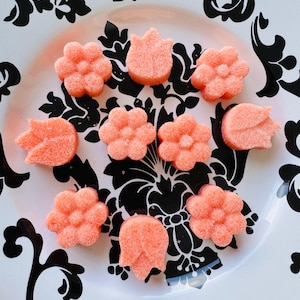 May include: A plate with a black and white floral design holds nine coral-coloured sugar cubes shaped like flowers and tulips.