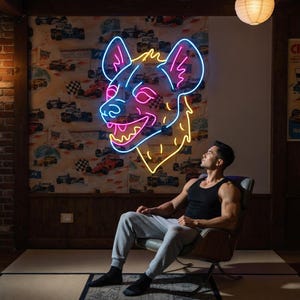 May include: A neon sign in the shape of a hyena's head, with pink and yellow lights, is mounted on a wall. The person is sitting in a chair, wearing a black tank top and gray sweatpants. The room has a vintage aesthetic with paper lanterns.