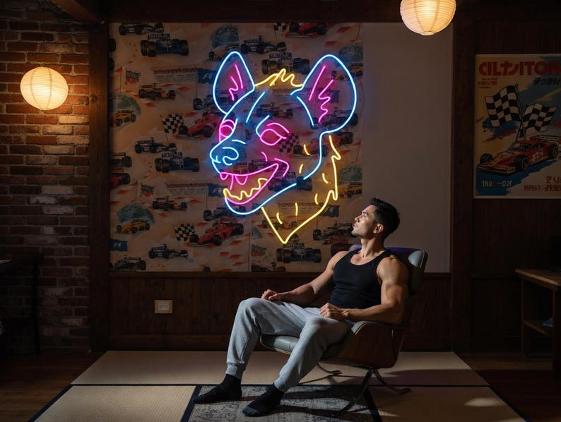 May include: A neon sign in the shape of a hyena's head, with pink and yellow lights, is mounted on a wall. The person is sitting in a chair, wearing a black tank top and gray sweatpants. The room has a vintage aesthetic with paper lanterns.