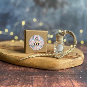 May include: A small glass bottle with a wooden cap and a woven cord, alongside a small brown box with a floral sticker. The box and bottle are on a wooden board. The sticker on the box reads "flicker bee".