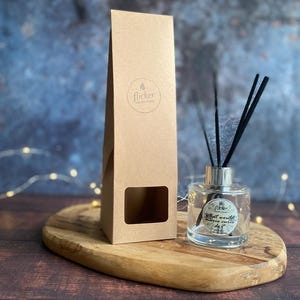 Könnte beinhalten: Eine klare Glas-Diffusorflasche mit schwarzen Schilfrohren und einem silbernen Deckel steht auf einem ovalen Holzbrett. Eine braune Pappschachtel mit Fenster und dem Wort "flicker" befindet sich neben dem Diffusor. Die Flasche trägt den Text "what would marie curie do?"