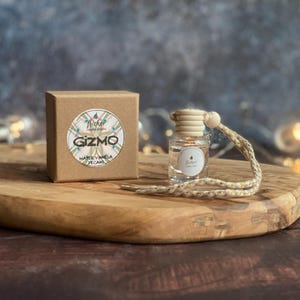 May include: A small glass bottle with a wooden cap and a decorative string, next to a brown cardboard box. The box has a circular label with the word "Gizmo" and the scent "Maple Vanilla Pecans".