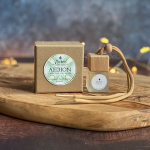 May include: A brown cardboard box with a white sticker that says "Flicker Candle Studio Aedion I Will Find You Again Rocksalt, Driftwood & Mint" and a small glass bottle with a wooden top and a brown cord attached to it. The bottle has a white sticker that says "Flicker Candle Studio".