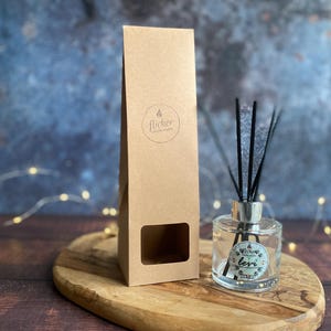 Könnte beinhalten: Ein klarer Glas-Diffusor für ätherische Öle mit schwarzen Stäbchen und einem silbernen Deckel steht auf einem Holzbrett. Eine braune Pappschachtel mit einem Fenster und dem Wort "flicker" befindet sich neben dem Diffusor. Der Diffusor hat ein Etikett mit der Aufschrift "levi".