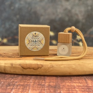 May include: A small, clear glass bottle with a wooden cap and a beige cord. The bottle is labeled "flicker candle studio" and contains a car air freshener with the scent "CHAOL WE WILL SEE EACH OTHER AGAIN BERGAMOT, ORANGE ALMOND".