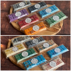 May include: A selection of colourful wax melt bars in shades like purple, red, orange, and blue, presented on a wooden serving board. Each bar is individually wrapped in clear plastic and labelled with a circular sticker.