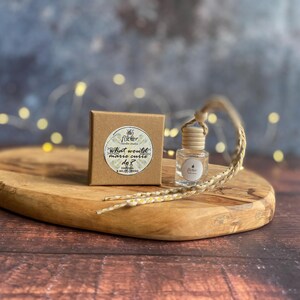 May include: A small glass bottle with a wooden cap and a woven cord, and a small brown box. The box has a circular sticker with text that reads "What would marie curie do?" and the brand name "Flicker candle studio". The items are on a wooden tray.