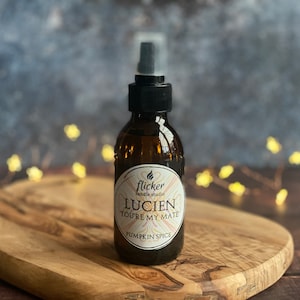 May include: A brown glass bottle with a black spray nozzle and a white label that reads "flicker candle studio LUCIEN YOU'RE MY MATE PUMPKIN SPICE".