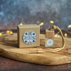 May include: A small brown box with a sticker that says "Flowey - The Woods - Illyrian Warriors - Cocoa Butter & Patchouli" and a small glass bottle with a wooden top and a brown string attached to it. The bottle has a label that says "Flowey".