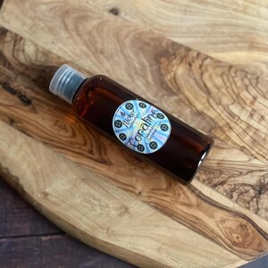 Pu&ograve; includere: Una bottiglia di vetro marrone con tappo argentato, riempita di liquido scuro, &egrave; appoggiata su un tagliere di legno. La bottiglia ha un'etichetta circolare con la scritta "Coraline" e un disegno blu e bianco.