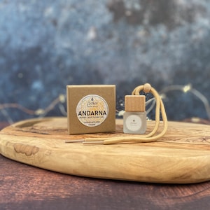 Może przedstawiać: Małe brązowe pudełko z tekstem "Flicker Candle Studio" i "Andarna Maybe I was saving you for later" oraz "Chocolate Chip Cookie". Mała szklana butelka z drewnianym korkiem i beżowym sznurkiem leży na drewnianej desce do krojenia.