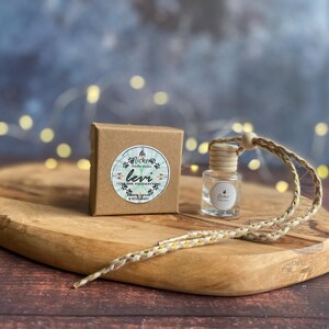 May include: A small, clear glass bottle with a wooden cap and a woven cord, next to a small brown box with a sticker that reads "Levi". The items are on a wooden chopping board.