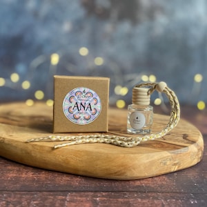 Könnte beinhalten: Eine kleine, klare Glasflasche mit einem Holzverschluss und einer geflochtenen Schnur, neben einer kleinen braunen Schachtel. Die Schachtel hat einen runden Aufkleber mit dem Text "ANA" und "FRUIT GUM". Die Artikel befinden sich auf einem Holzservierbrett.